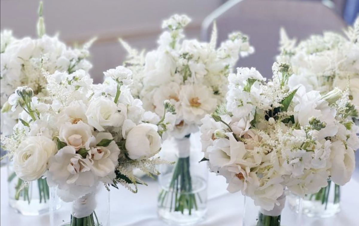 White wedding party bouquets of garden roses, ranunculus, stock and astilbe standing in glass vases